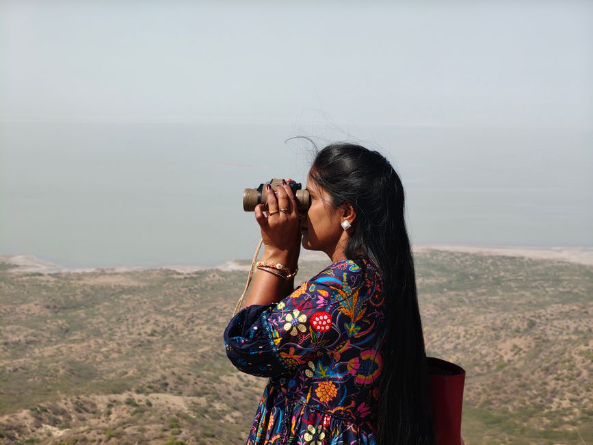 Woman using binoculars to observe distant landscape from an elevated point.